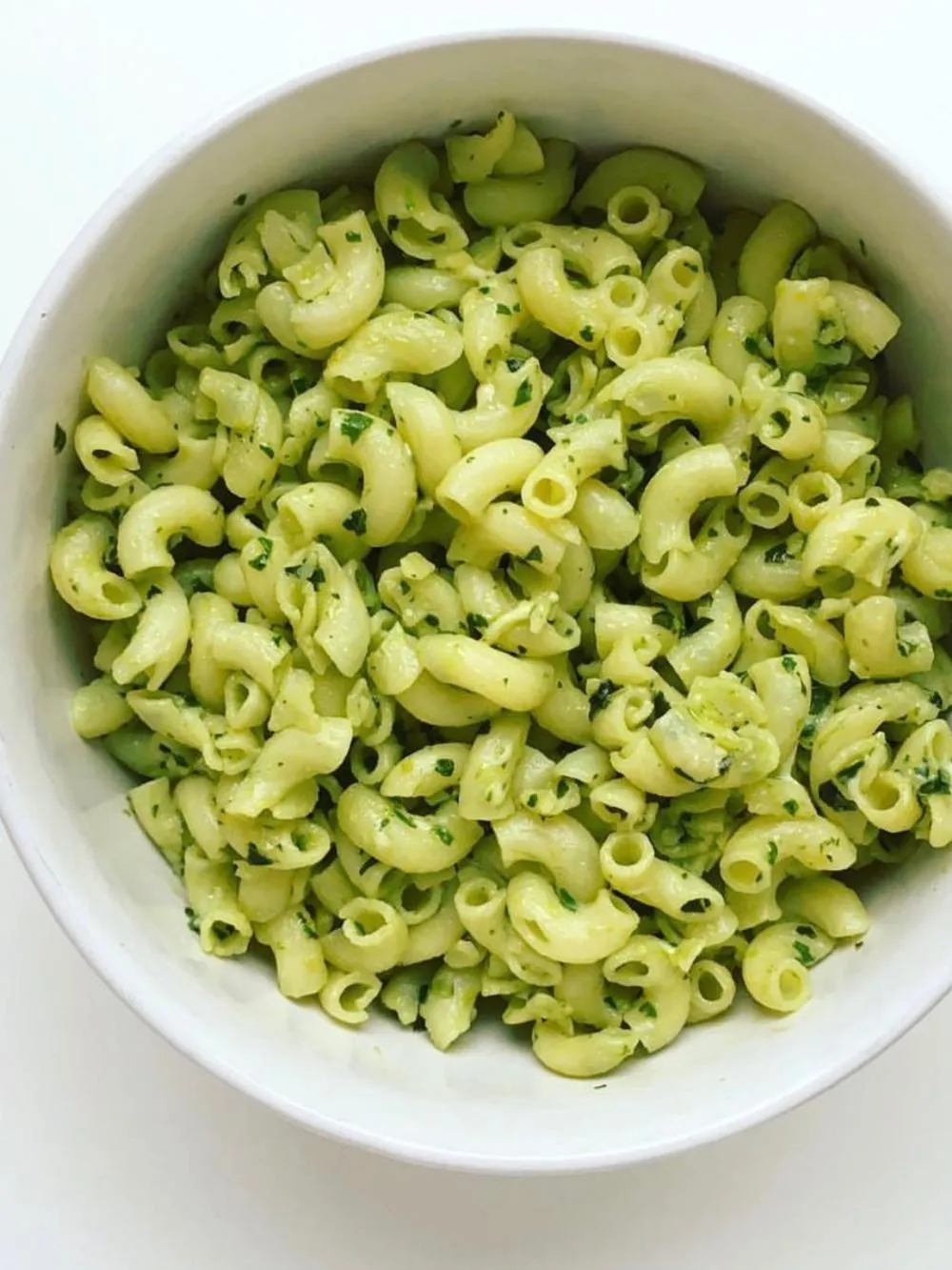 a white bowl full of macaroni noodles in a pesto on a white table