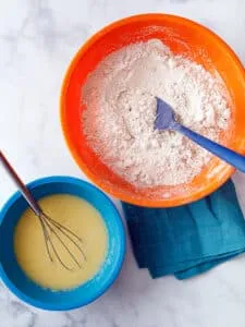 orange bowl with dry ingredients and a blue bowl with wet ingredients for oat flour biscuits
