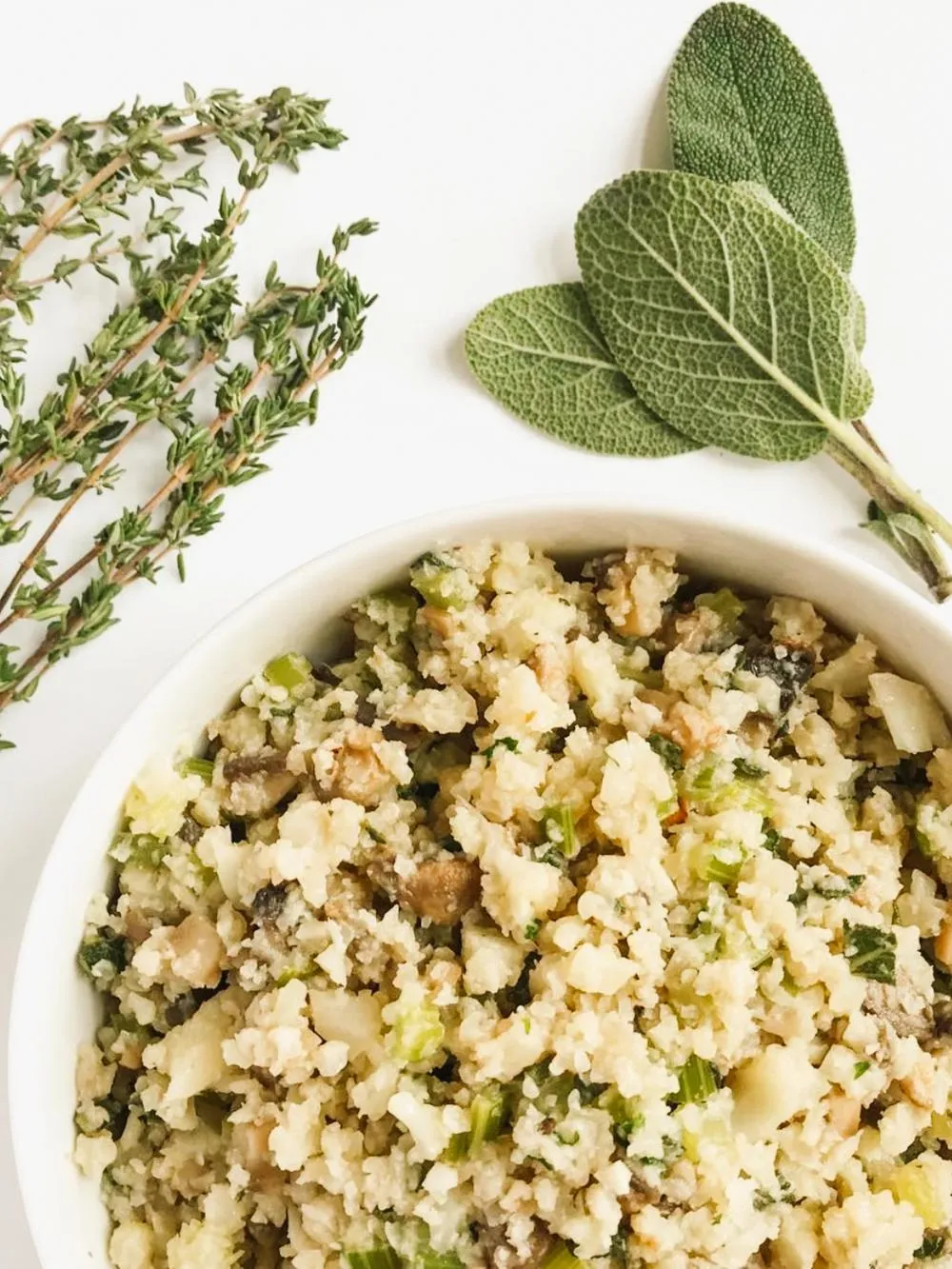 a white bowl of grain free thanksgiving stuffing surrounded by fresh sage and thyme