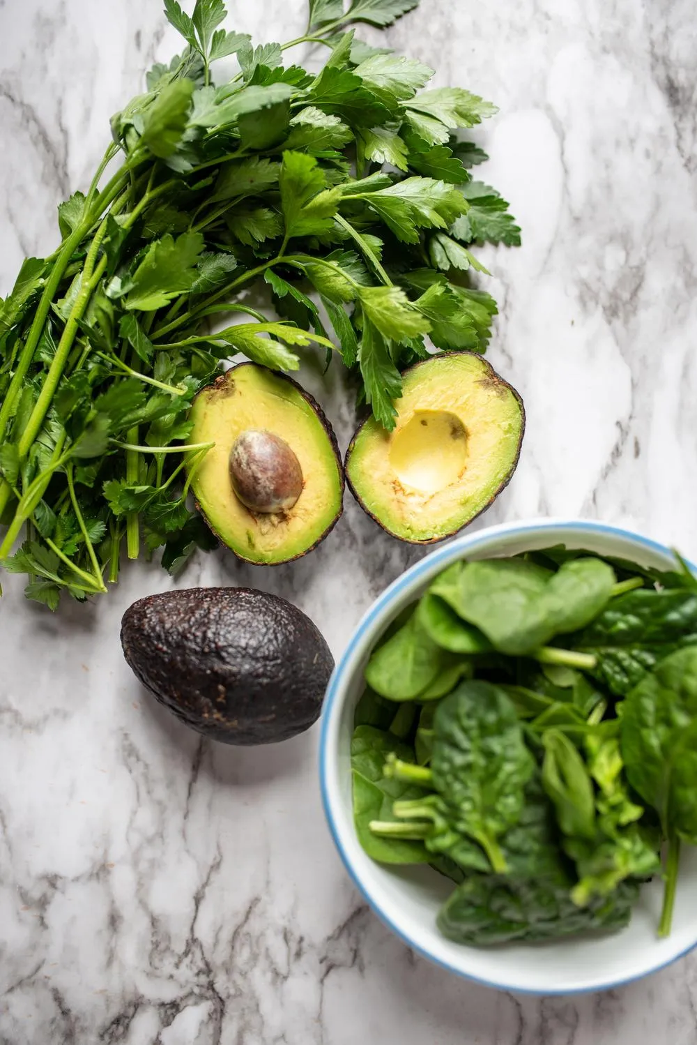 a bowl of spinach next to an avocado and bunch of parsley