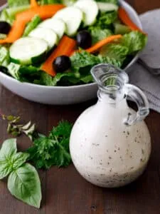 a glass bottle of salad dressing next to a bowl of salad