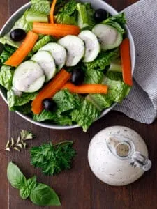 A bowl of salad sitting on a table next to a bottle of dressing