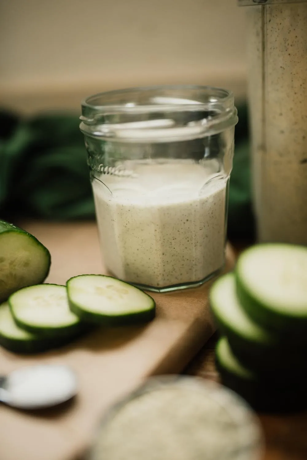 a cup of prepared alkaline salad dressing with the blender cup behind and chopped cucumbers in front