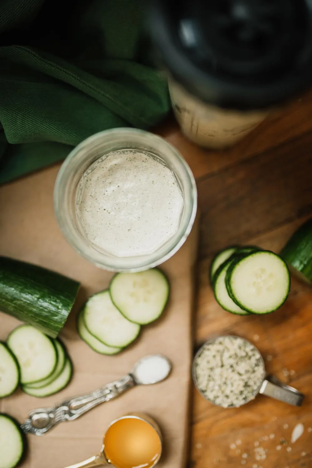 a jar of alkaline cucumber hemp dressing next to all the ingredients: sliced cucumbers, salt, ACV, and hemp hearts