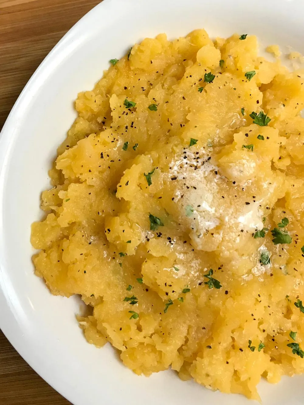 a white bowl of mashed rutabaga with melted butter and fresh chopped chives